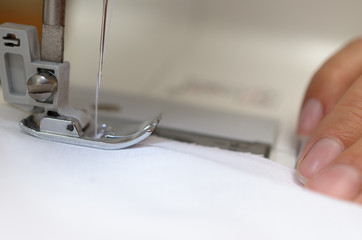 Hands seamstresses with white material behind the sewing machine.