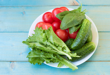 Tomatoes, cucumbers, spinach and lettuce leaves on a white plate.
