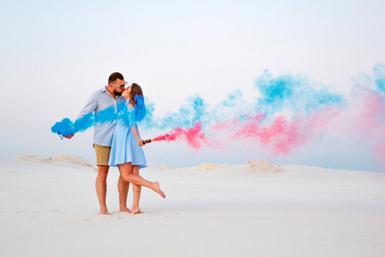 young couple kissing and holding colored smoke in hands, romantic couple with blue color and red color smoke bomb on beach..