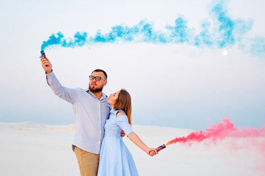 young couple  standing on a sand and holding colored smoke bomb , romantic couple with blue color and red color smoke bomb on beach
