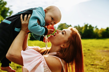 Obraz premium a red-haired woman holds her young son in her arms at sunset in a green Park. They eat an Apple together.