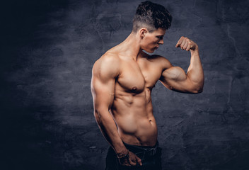Fototapeta na wymiar Strong shirtless young man model with nice muscular body showing his bicep at a studio.