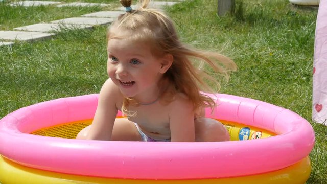Child plays and having fun in inflatable rubber pool on green lawn at a sunny day