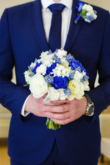 Groom holding wedding bouquet with fresh white and blue flowers roses