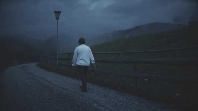 Senior woman walks alone on the lonely road of me mountains. Mist in the nigh