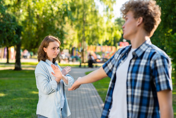 Young man in summer in a park outdoors. Tries to get acquainted with a beautiful girl. The girl gestures to show no. Unwillingness to talk. The concept of dating in the city.