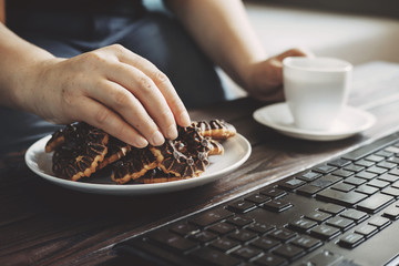 Unhealthy snack at work time. Woman eating chocolate cookies and drinking coffee at workplace. High calorie, fattening junk food, weight gain