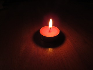 A small red tealight candle lit in a dark room on a table