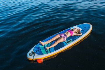 Young woman woman relaxes lying on back, on paddle board, at sea, view from above