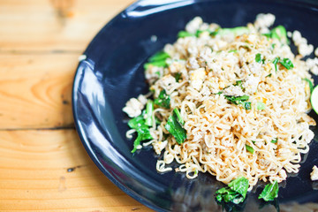 Close-up stir fried Mama or Thai phat  fried noodles with sliced lemon and vegetables in black dish, On the Oak wooden table background.