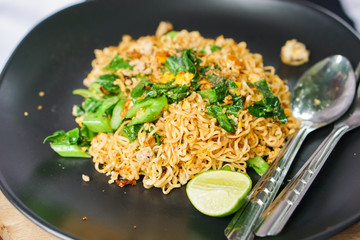 Close-up stir fried Mama or Thai phat  fried noodles with sliced lemon and vegetables in black dish, On the Oak wooden table background.