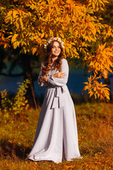 Obraz na płótnie Canvas a woman in a long white dress closed her eyes and stands on the background of the lake and autumn trees