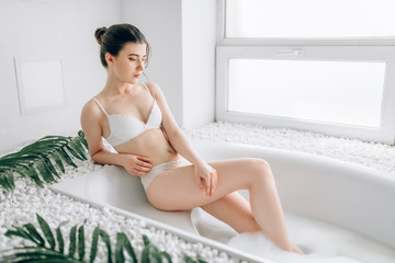 Obraz na płótnie Canvas Woman in white underwear sitting in bath with foam