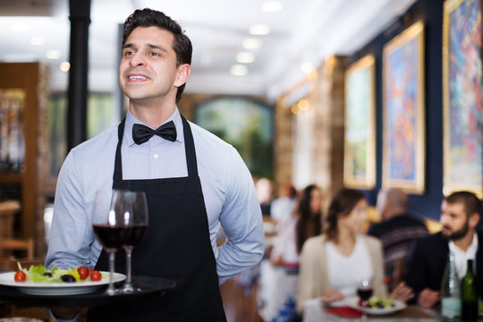 Smiling waiter with serving tray in restaurant