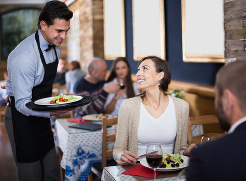 Waiter  male bringing food for man and woman guests