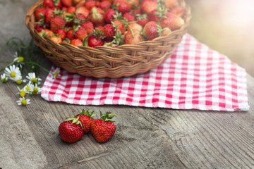 three strawberries on a wooden old background and a basket of berries