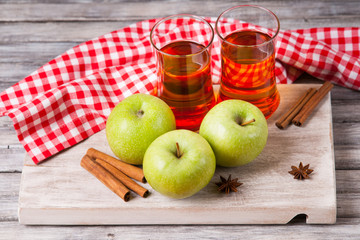 Apple juice in glasses, spices and apples on wooden cutting table 