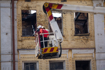 Naklejka premium Ladder cart with the fire against the background of the facade of the burned building. Fire