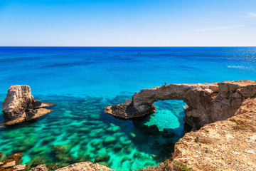 Woman on the beautiful natural rock arch near of Ayia Napa, Cavo Greco and Protaras on Cyprus island, Mediterranean Sea. Legendary bridge lovers. Amazing blue green sea and sunny day.