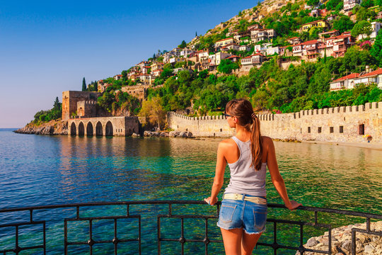 Young woman look on ancient shipyard from Kizil Kule tower in Alanya peninsula, Antalya district, Turkey, Asia. Famous tourist destination with high mountains. Part of ancient old Castle