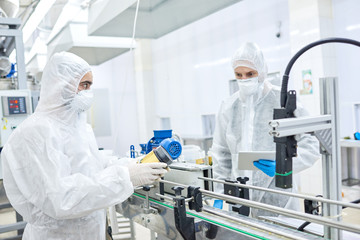 Production workers in protective clothing operating at conveyor belt holding ready package with sports nutrition.