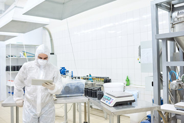 Sports nutrition production worker in protective clothing focused on using tablet computer. 