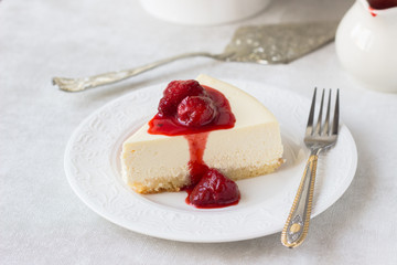 Classical vanilla cheesecake (New York cheesecake) with strawberry sauce and rosemary on white plate and light background