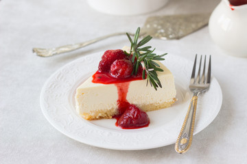 Classical vanilla cheesecake (New York cheesecake) with strawberry sauce and rosemary on white plate and light background