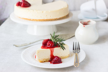 Classical vanilla cheesecake (New York cheesecake) with strawberry sauce and rosemary on white plate and light background