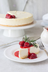 Classical vanilla cheesecake (New York cheesecake) with strawberry sauce and rosemary on white plate and light background