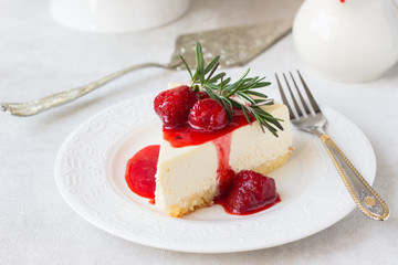 Classical vanilla cheesecake (New York cheesecake) with strawberry sauce and rosemary on white plate and light background