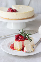 Classical vanilla cheesecake (New York cheesecake) with strawberry sauce and rosemary on white plate and light background