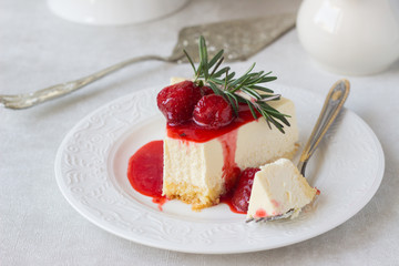 Classical vanilla cheesecake (New York cheesecake) with strawberry sauce and rosemary on white plate and light background