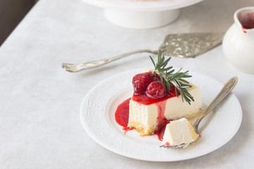 Classical vanilla cheesecake (New York cheesecake) with strawberry sauce and rosemary on white plate and light background