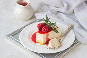 Classical vanilla cheesecake (New York cheesecake) with strawberry sauce and rosemary on white plate and light background