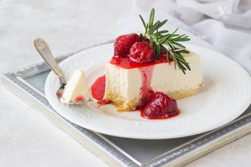 Classical vanilla cheesecake (New York cheesecake) with strawberry sauce and rosemary on white plate and light background