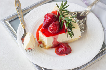 Classical vanilla cheesecake (New York cheesecake) with strawberry sauce and rosemary on white plate and light background
