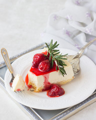 Classical vanilla cheesecake (New York cheesecake) with strawberry sauce and rosemary on white plate and light background