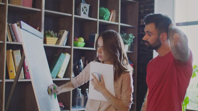 Man and woman discussion business solutions. Colleagues writing business plan on flipchart in office. Creative team working on white marker board in studio. Marketers working on marketing strategy