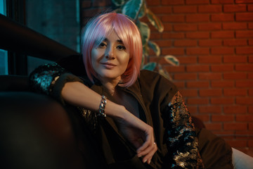 Girl with pink hair sitting relaxed on a leather sofa