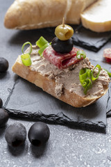 Bread with pate on the black slate tray decorated with black and green olives