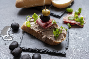 Bread with pate on the black slate tray decorated with black and green olives