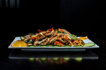 Chinese cuisine, boiled beef with cucumber and tomato in white plate, on black background