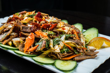 Chinese cuisine, boiled beef with cucumber and tomato in white plate, on black background