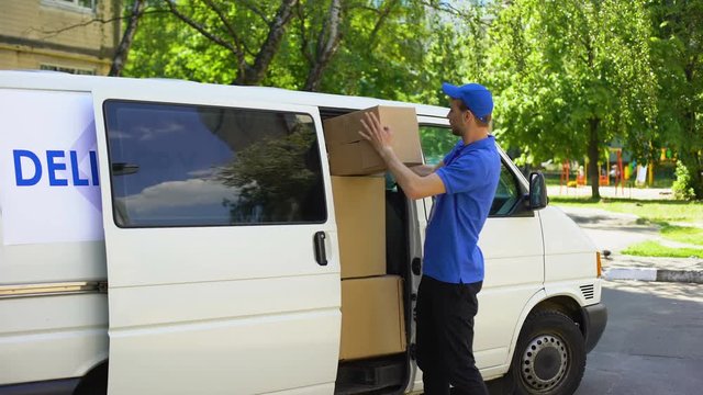 Postal office worker taking parcel box from delivery van and showing thumbs up