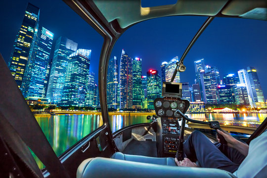 Helicopter cockpit interior flying on the central business district from marina bay waterfront promenade by the bayfront south jetty. Singapore cityscape illuminated at night.