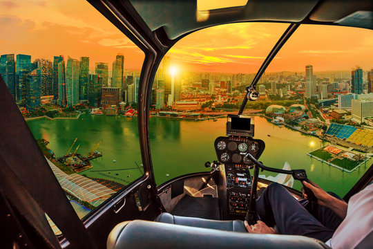 Helicopter cockpit interior flying on Singapore marina bay panorama of financial district skyscrapers at sunset on the harbor skyline. Aerial Singapore cityscape at twilight time.