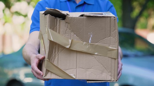 Male courier showing damaged box, cheap parcel delivery, poor shipment quality