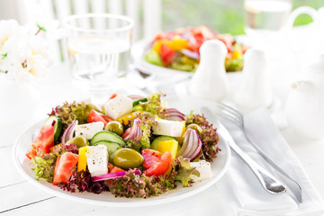 Greek salad. Fresh vegetable salad with tomato, onion, cucumber, pepper, olives, lettuce and feta cheese. Greek salad on plate on white table