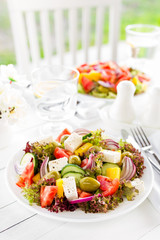 Greek salad. Fresh vegetable salad with tomato, onion, cucumber, pepper, olives, lettuce and feta cheese. Greek salad on plate on white table